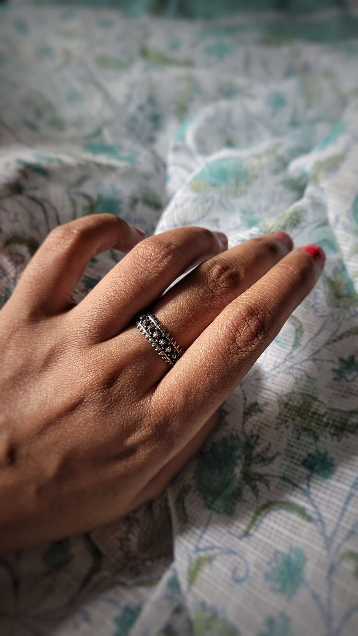 Hand with Aadi ring on a patterned fabric background