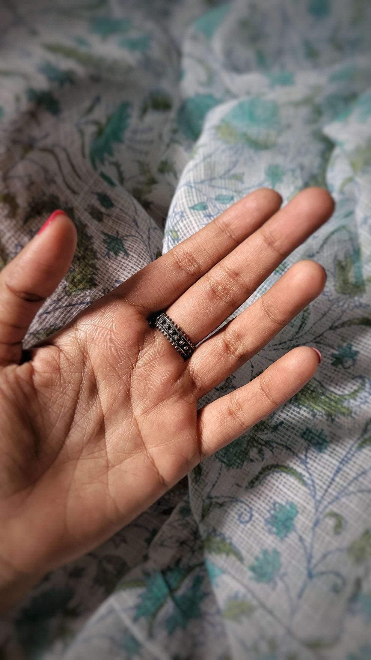 Hand wearing Aadi ring with small stones on a patterned fabric background