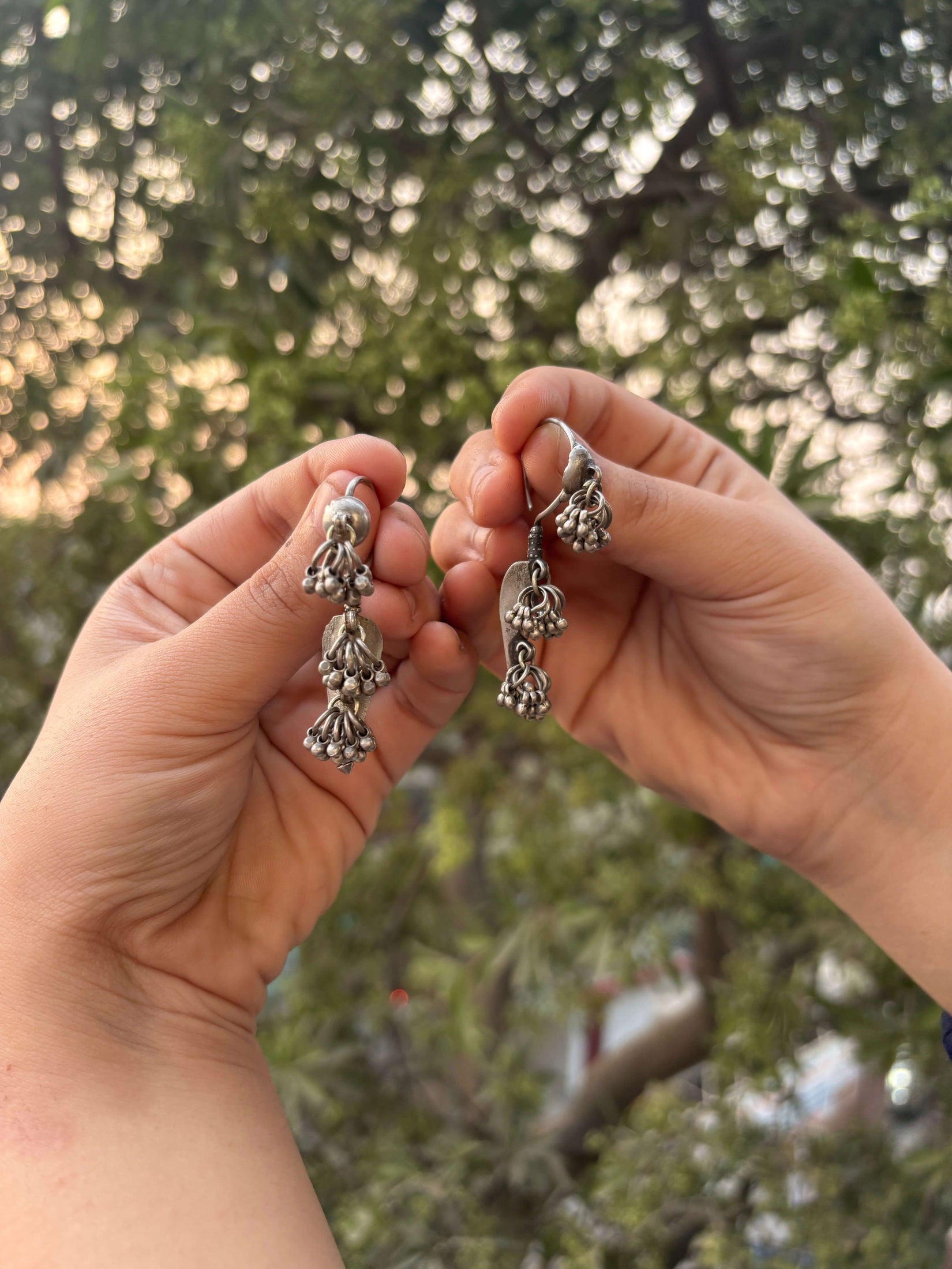 Two hands holding silver earrings against a blurred natural background