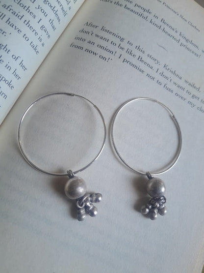 A pair of silver-tone hoop earrings with small pearl-like beads and tiny metallic charms, displayed on the pages of an open book.