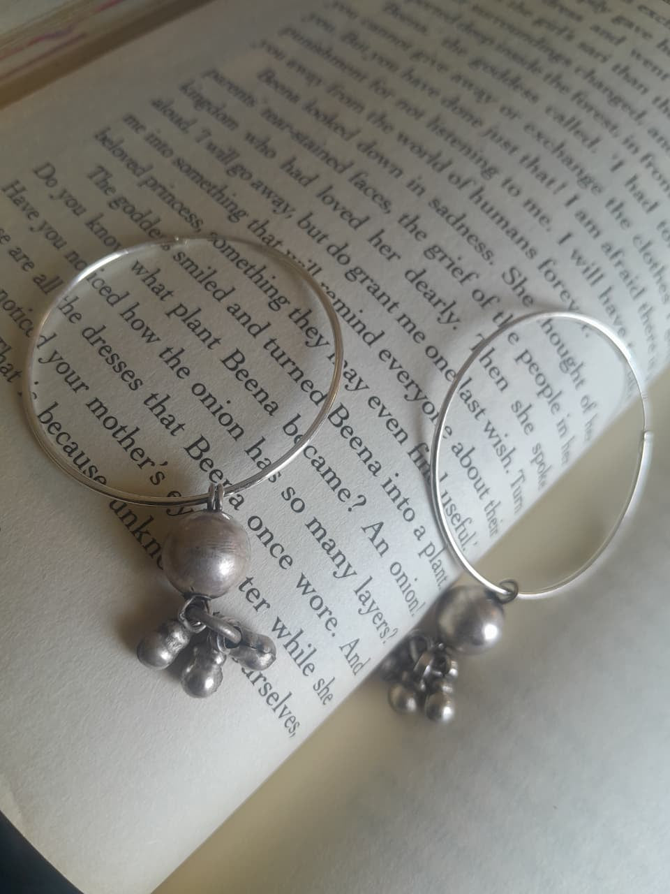 Silver hoop earrings with dangling silver beads and small bells, displayed on the pages of an open book.