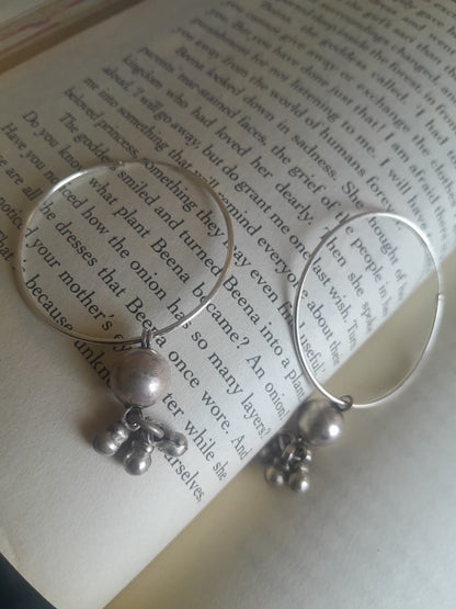 Silver hoop earrings with dangling silver beads and small bells, displayed on the pages of an open book.