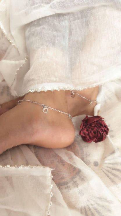 Close-up of a foot wearing a silver anklet with a red flower accessory, on a blurred background.
