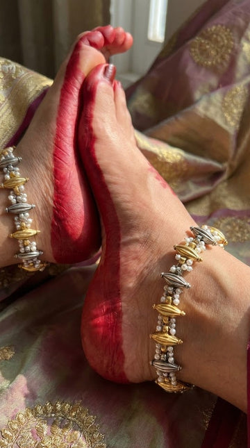 Close-up of feet with gold and silver beaded anklets on a patterned fabric background
