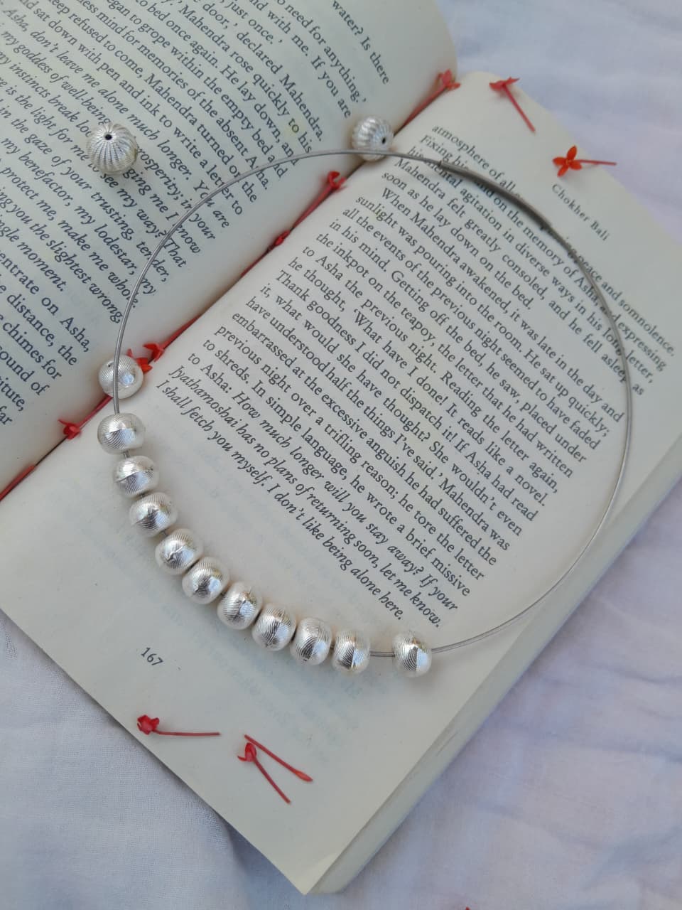 Silver beaded necklace on an open book with red bookmarks.