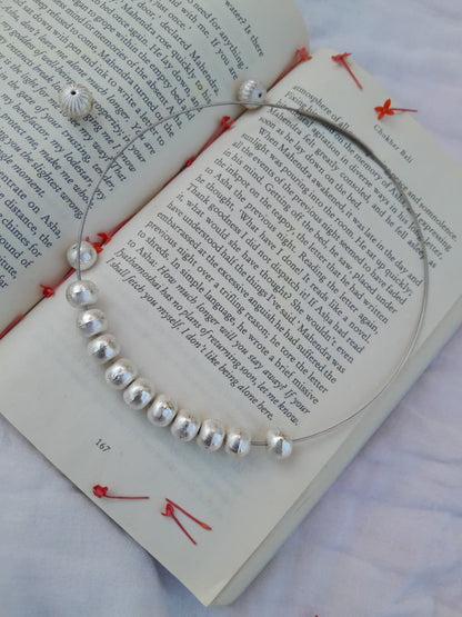 Silver beaded necklace on an open book with red bookmarks.