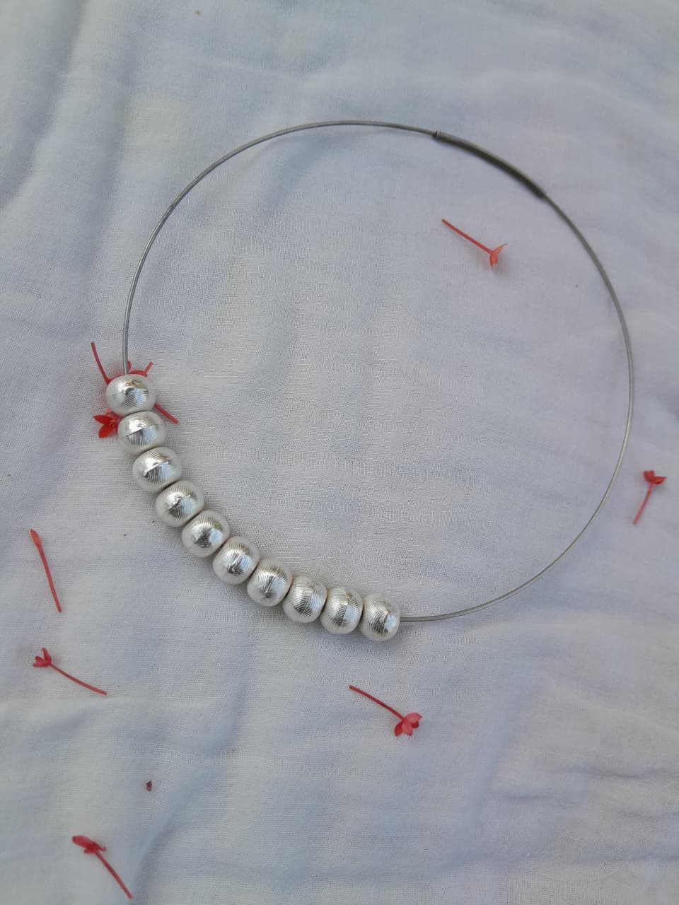 Silver beaded necklace on a white fabric background with red pins