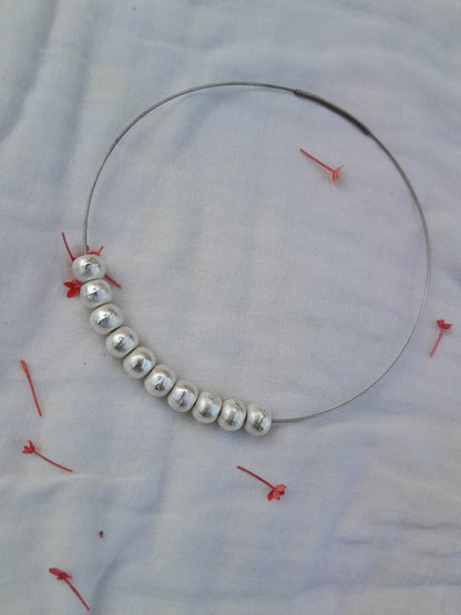 Silver beaded necklace on a white fabric background with red pins