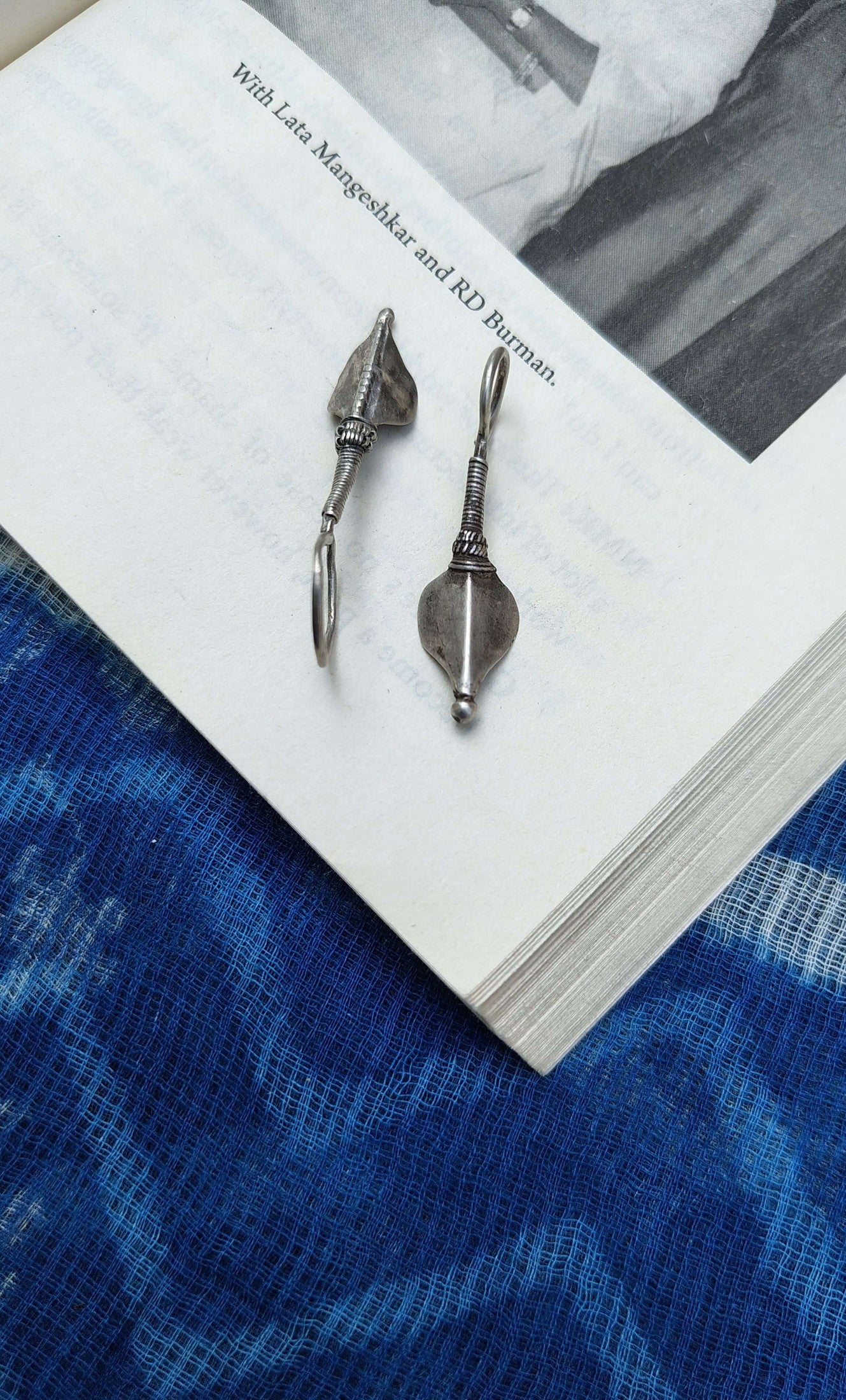 Two silver earrings on a book with a blue fabric background