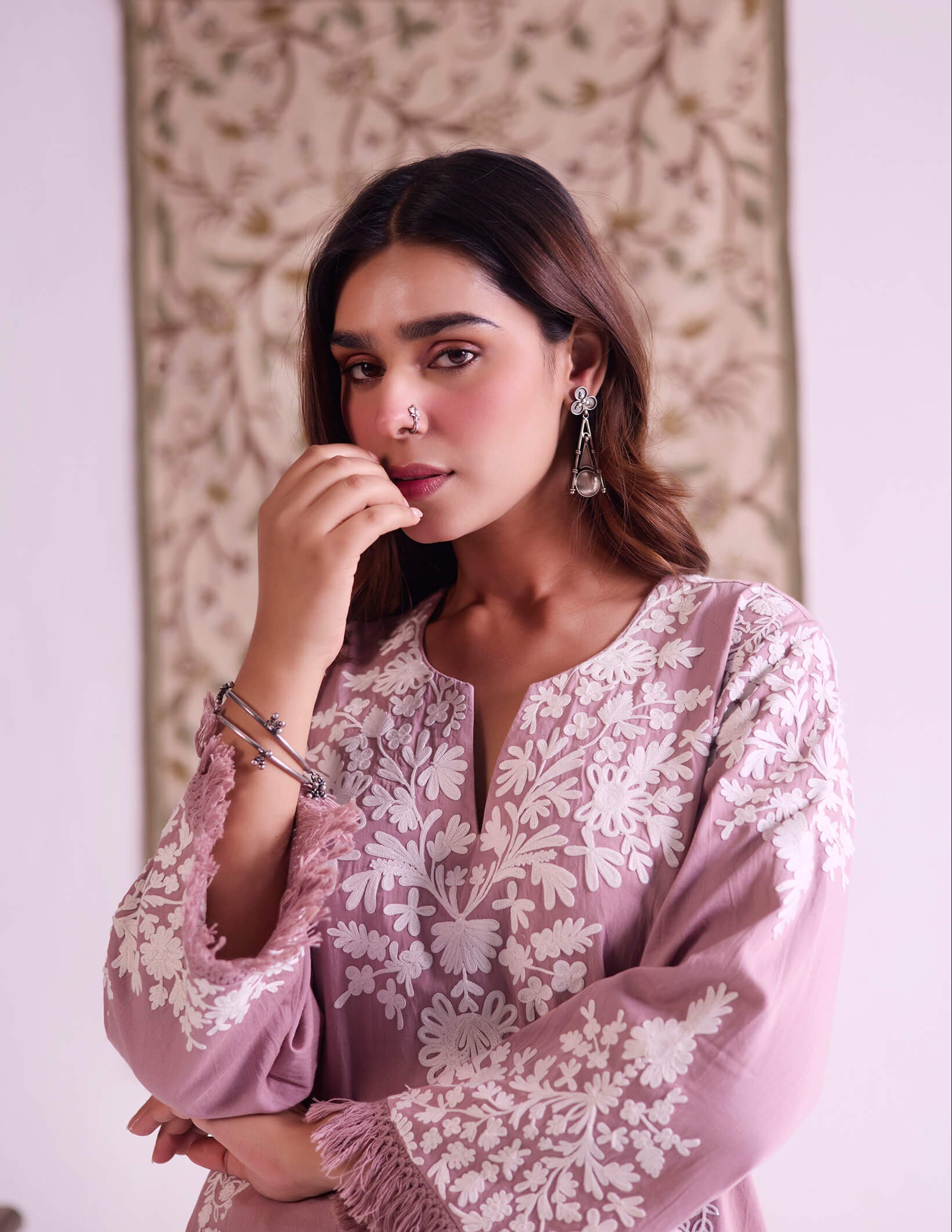 Woman wearing a pink embroidered dress with a decorative background