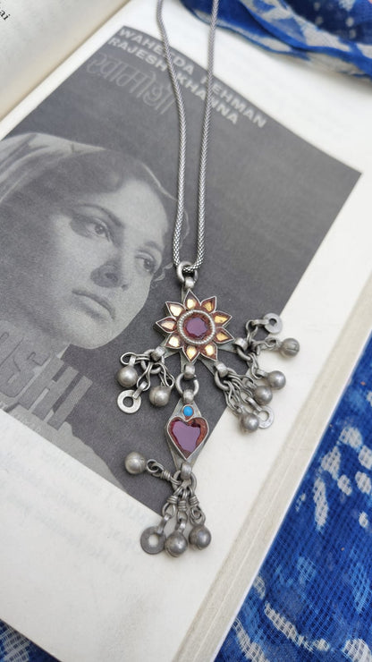 Side view of a rare vintage silver maximalist pendant — hand-cut glass sunflower with red centre and yellow petals, maroon glass heart dangler, turquoise accent, dense ghungroos and geometric danglers throughout. Available with or without chain. Shop Sadabahaar Jewelry.