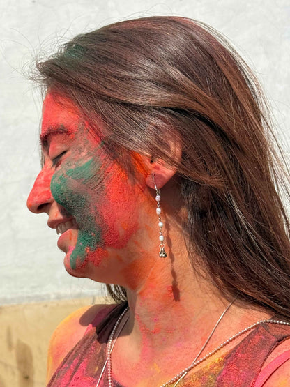 Woman with colorful face paint, likely from Holi festival, with silver pearl earrings against a neutral background.