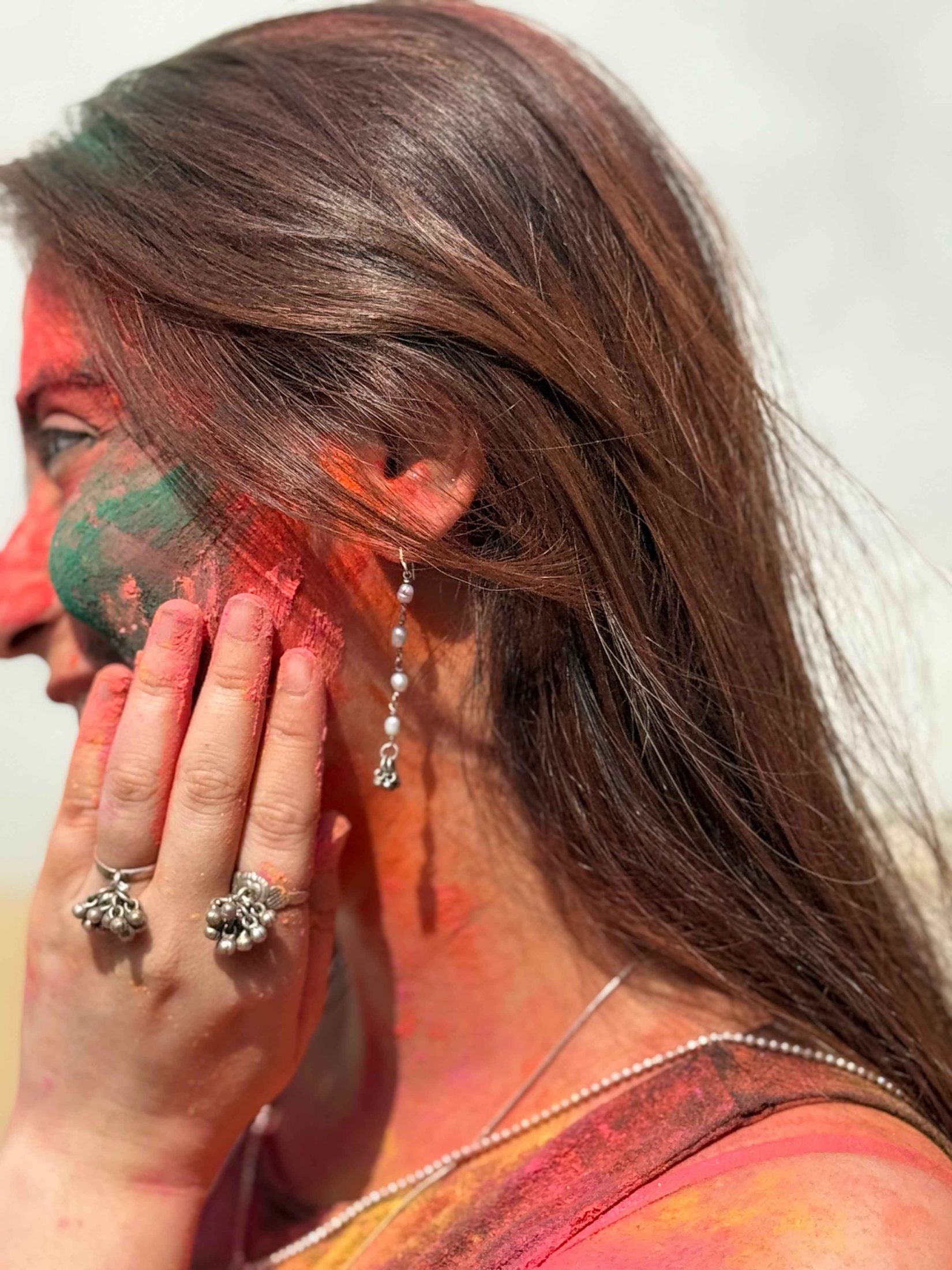 Woman with colorful face paint and pearl earrings, participating in Holi festival.