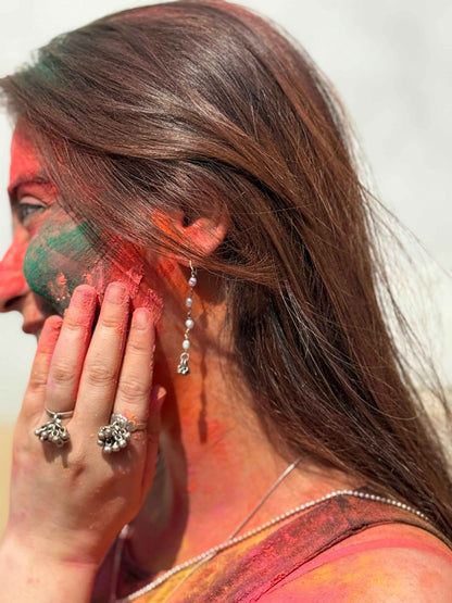 Woman with colorful face paint and pearl earrings, participating in Holi festival.