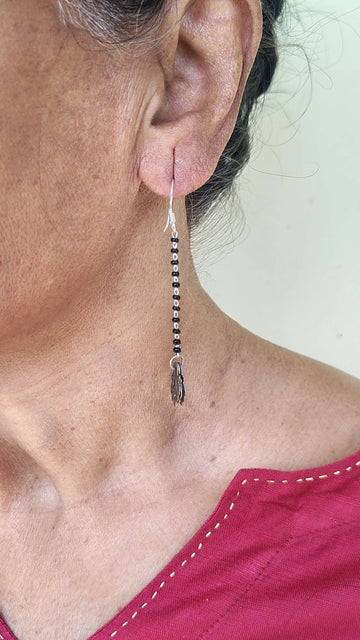 Close-up of an ear wearing a black beaded earring with a plain background