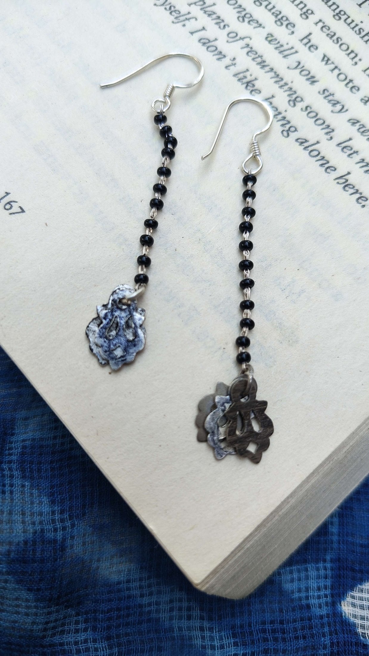 Pair of earrings with black beads and floral designs on a book page | Sadabahaar Jewelry