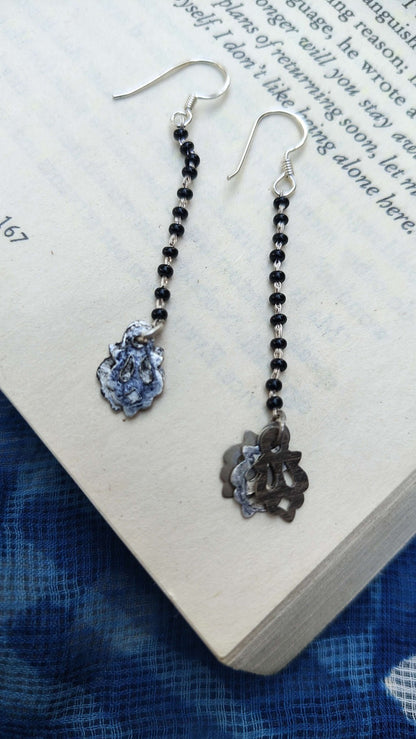 Pair of earrings with black beads and floral designs on a book page | Sadabahaar Jewelry