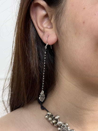 Close-up of an earring with a black thread and silver chain on a person's ear.