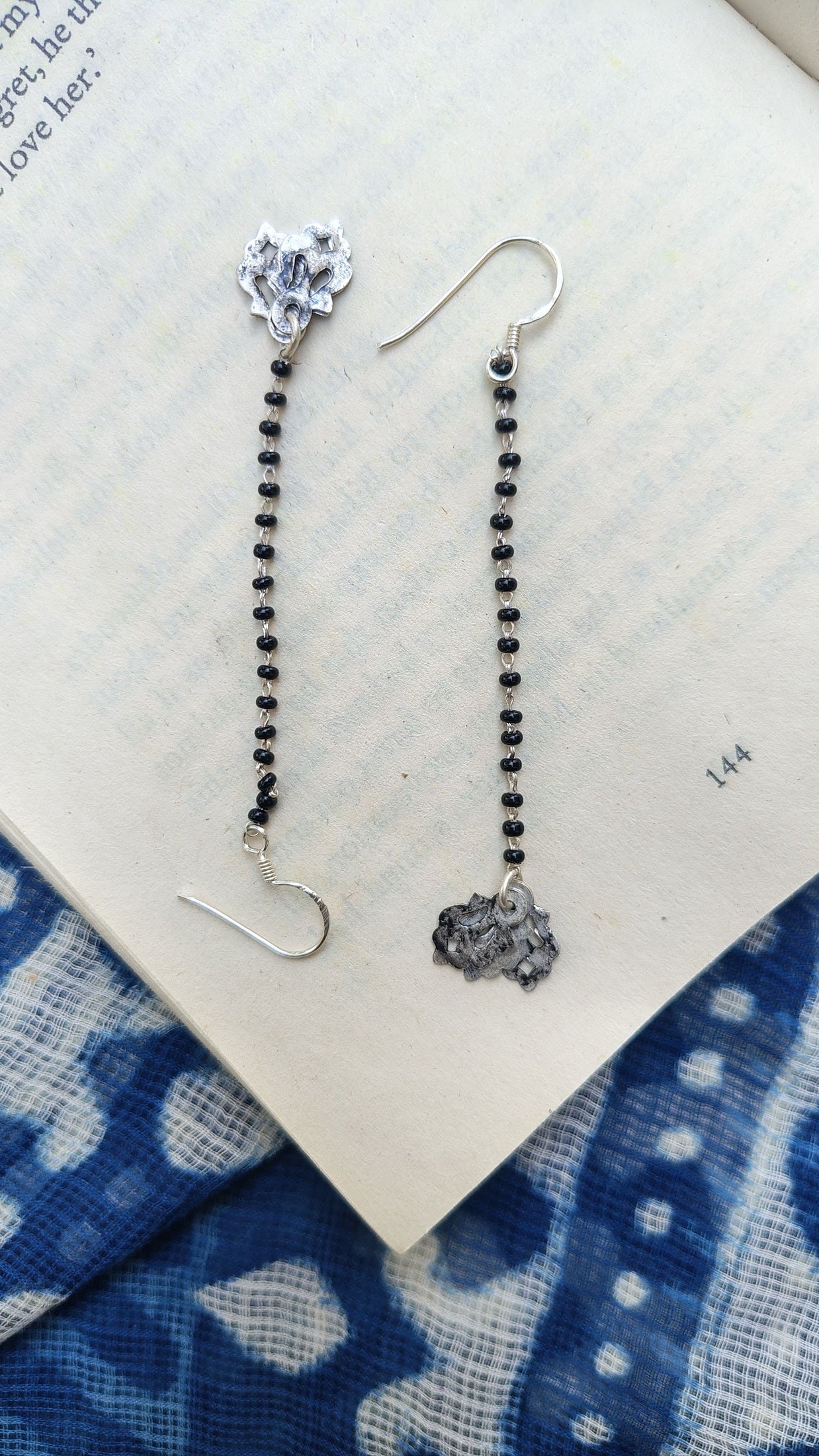 Pair of silver earrings with black beads on a blue and white patterned fabric background.