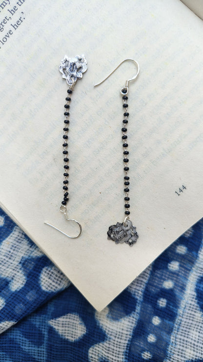 Pair of silver earrings with black beads on a blue and white patterned fabric background.