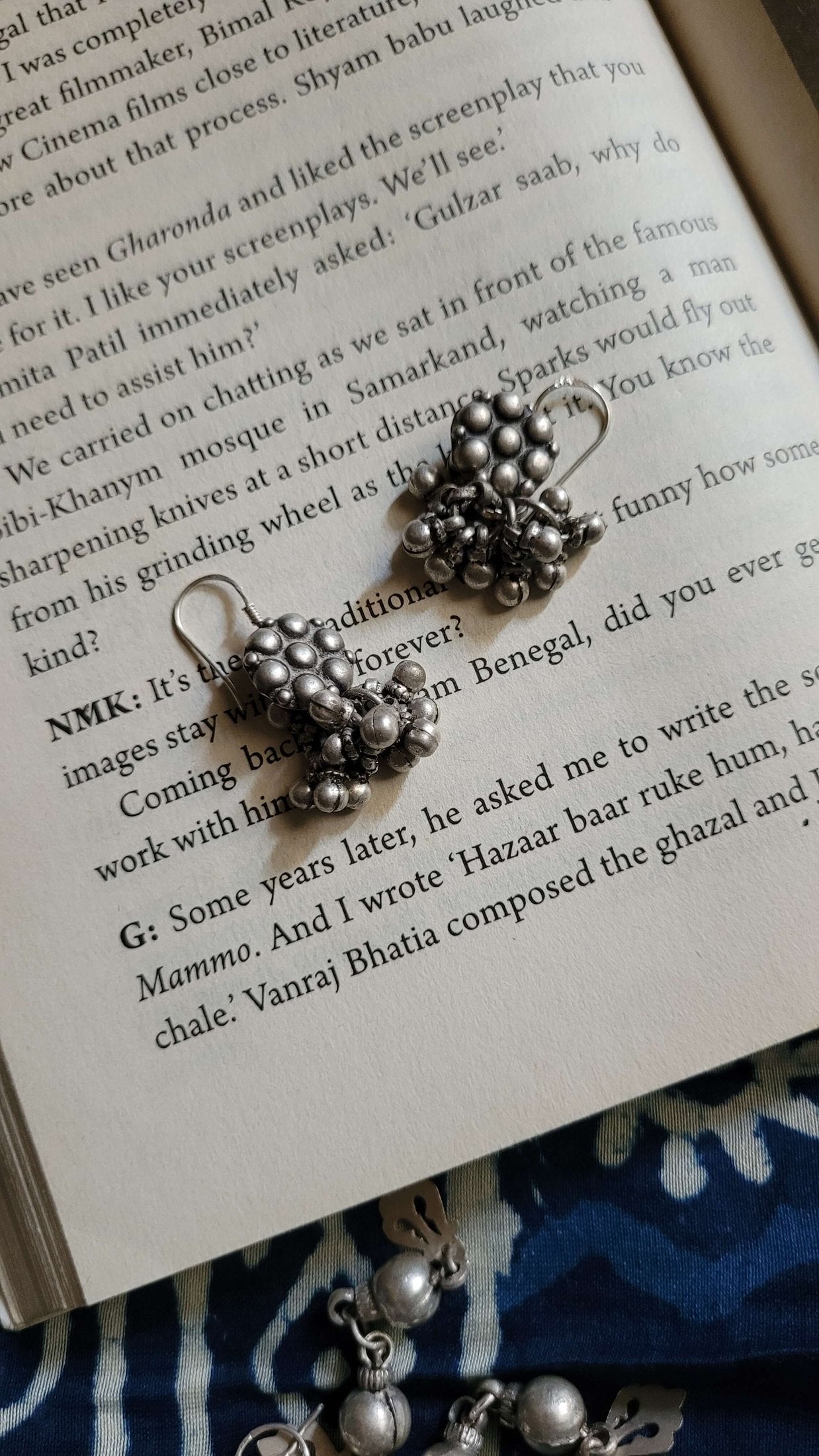 Silver earrings on an open book with a blue fabric background