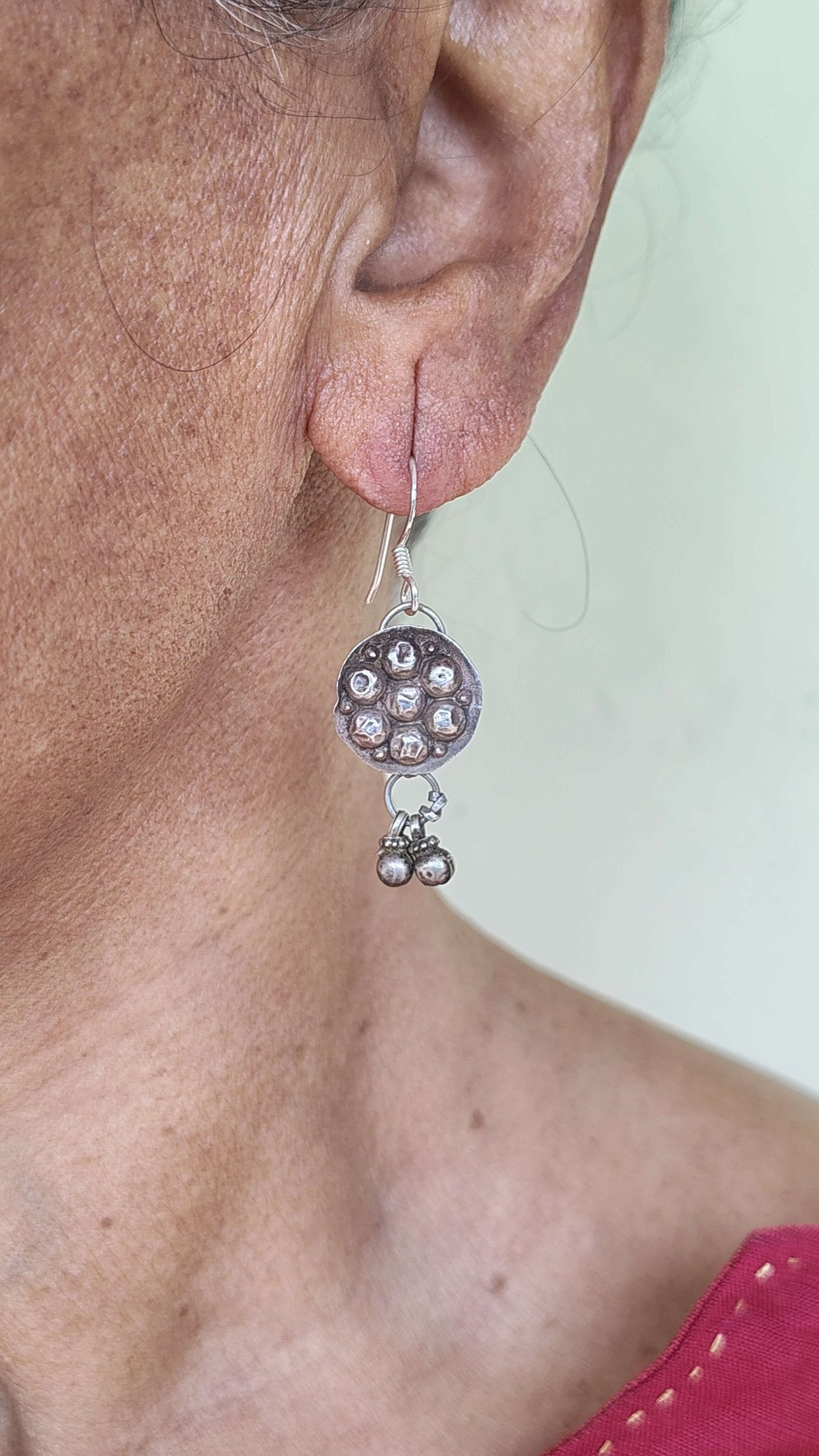 Close-up of an ear wearing a silver earring with a pink background