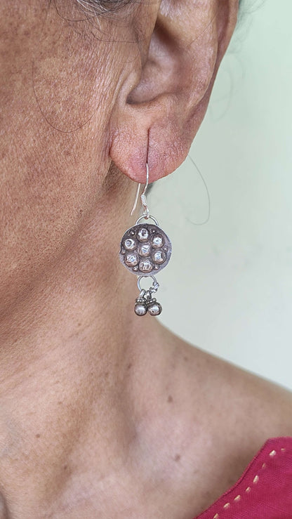 Close-up of an ear wearing a silver earring with a pink background