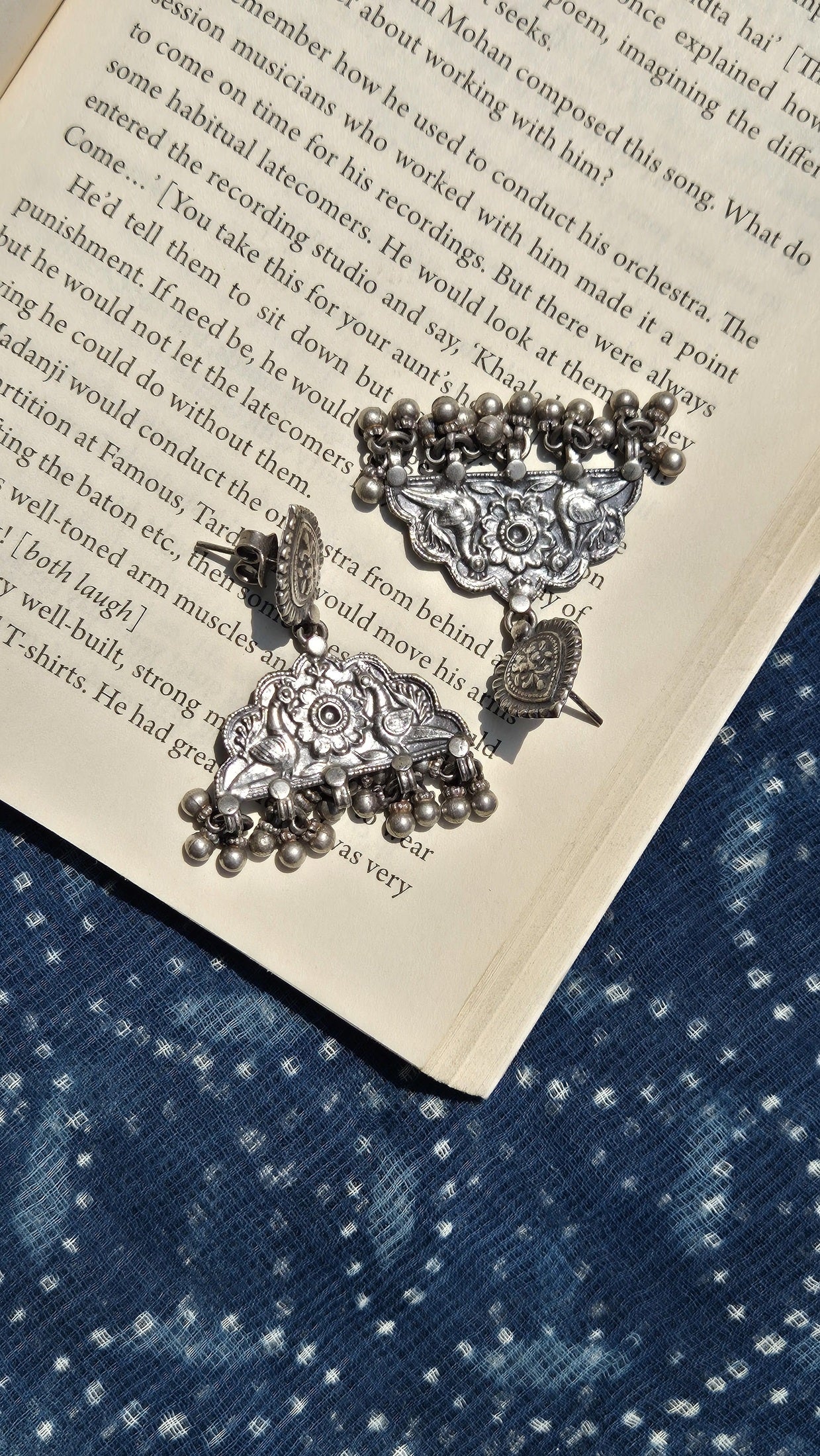 Decorative silver earrings on an open book with a blue fabric background