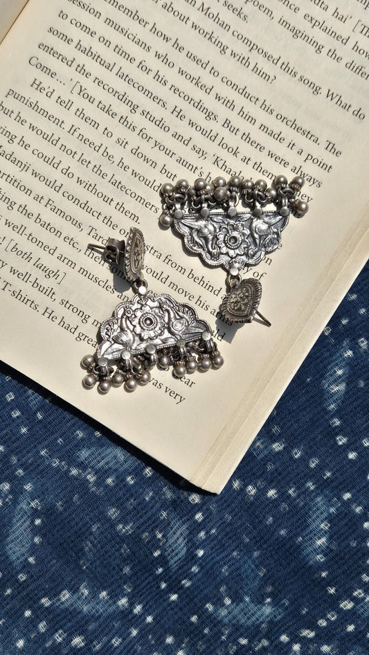 Decorative silver earrings on an open book with a blue fabric background