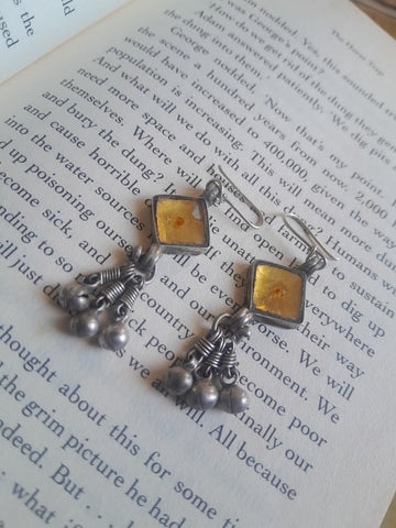 A pair of handmade silver-toned dangle earrings with square amber-yellow inlay and dangling silver beads, displayed on an open book page.