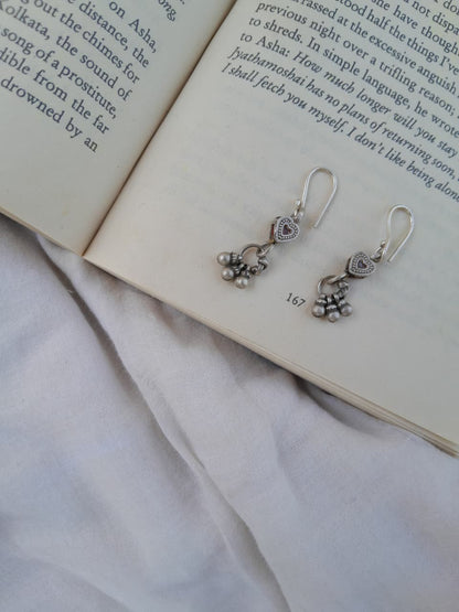 Silver earrings with heart and floral designs on an open book