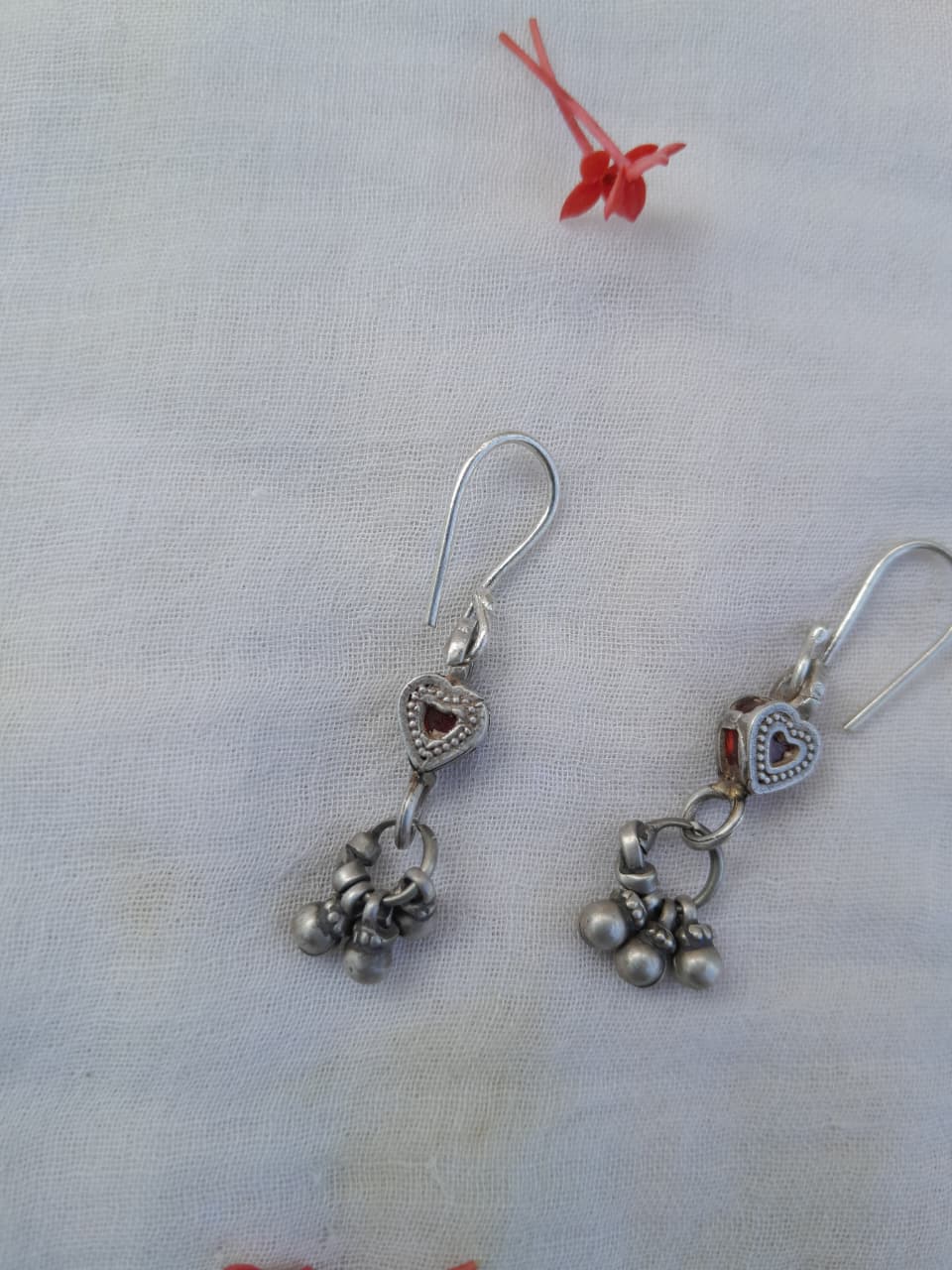 Silver earrings with heart and bell charms on a light fabric background