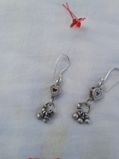 Silver earrings with heart and bell charms on a light fabric background