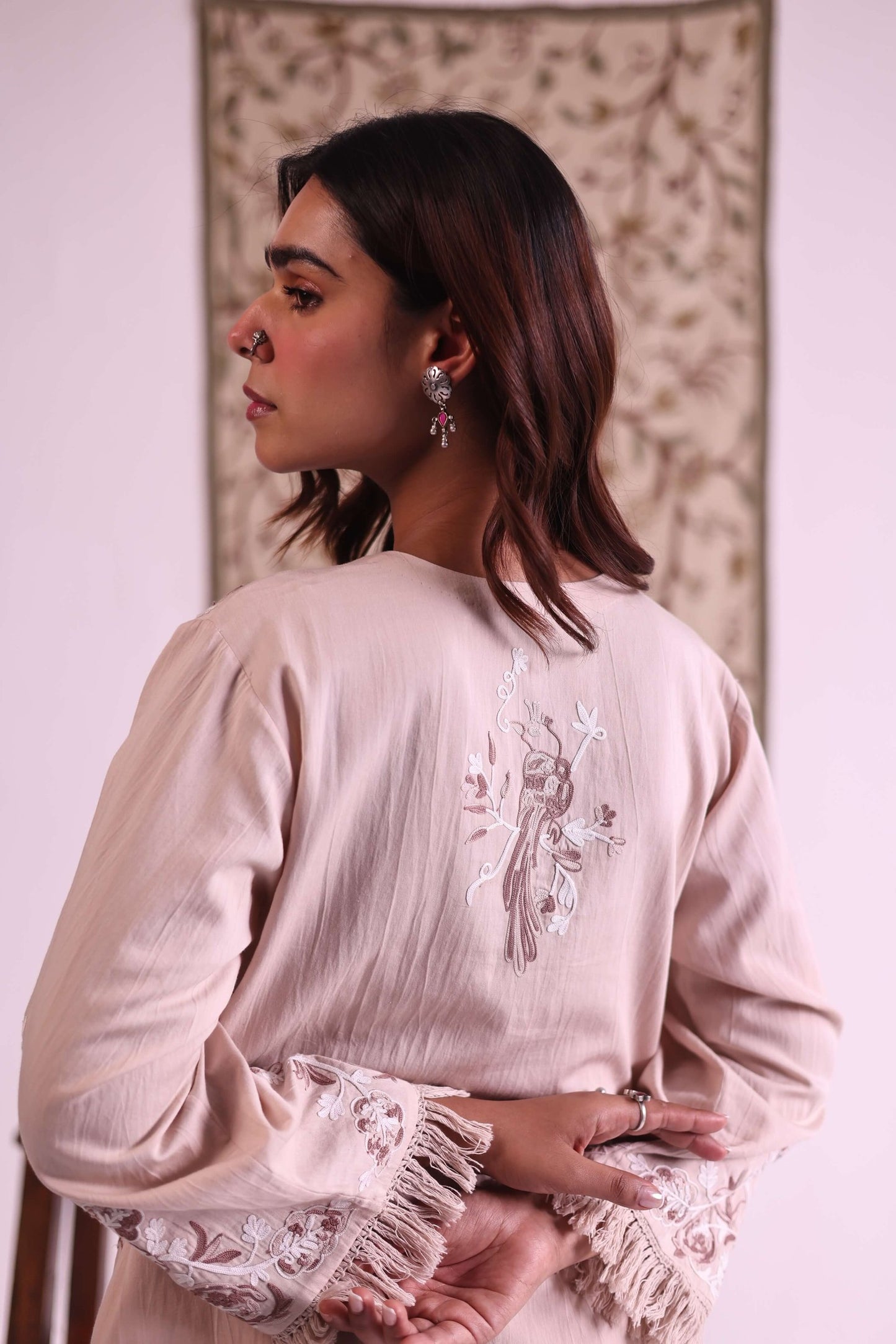 Woman wearing a beige embroidered dress with floral patterns.