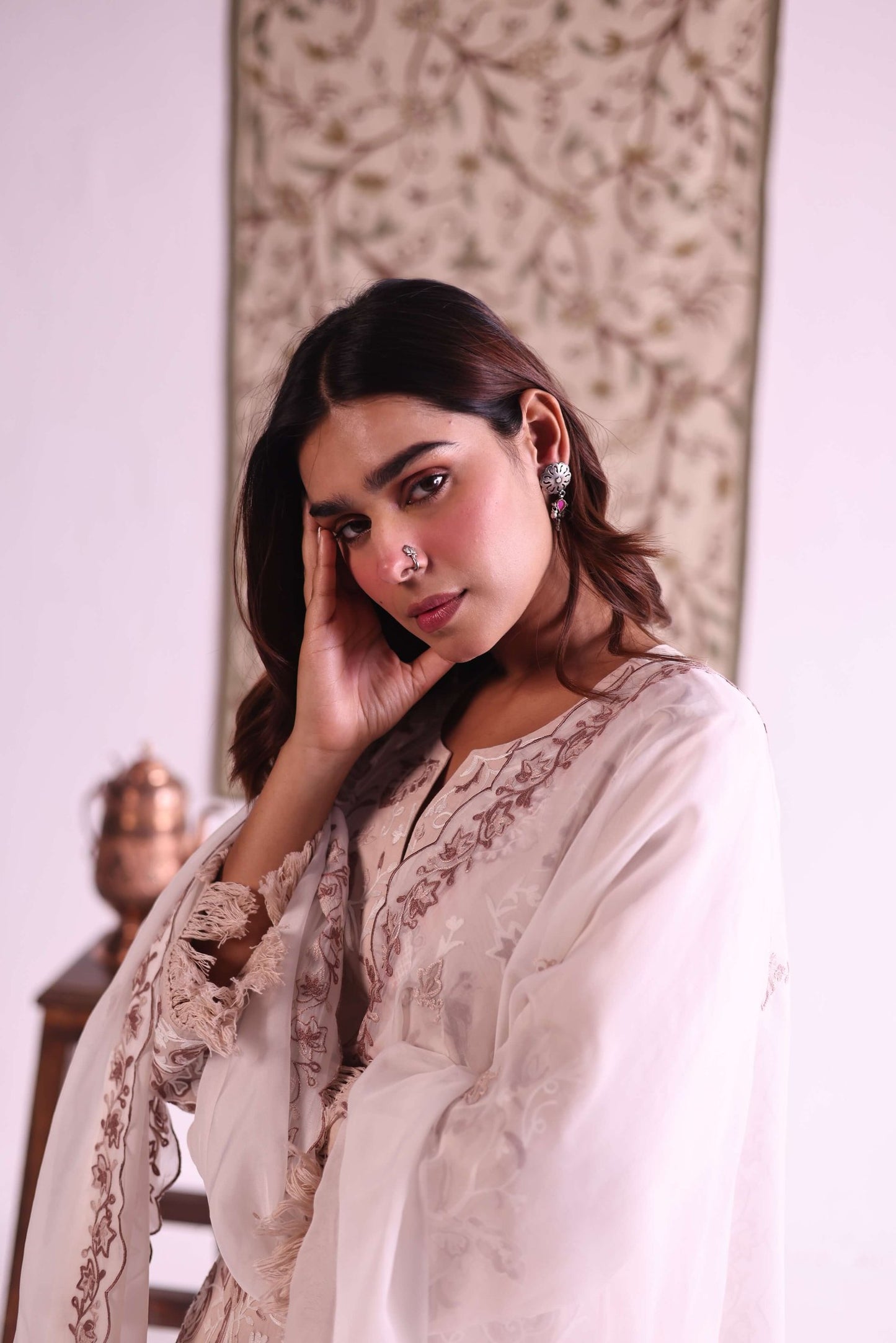 Woman in a white traditional outfit with intricate patterns, posing indoors.