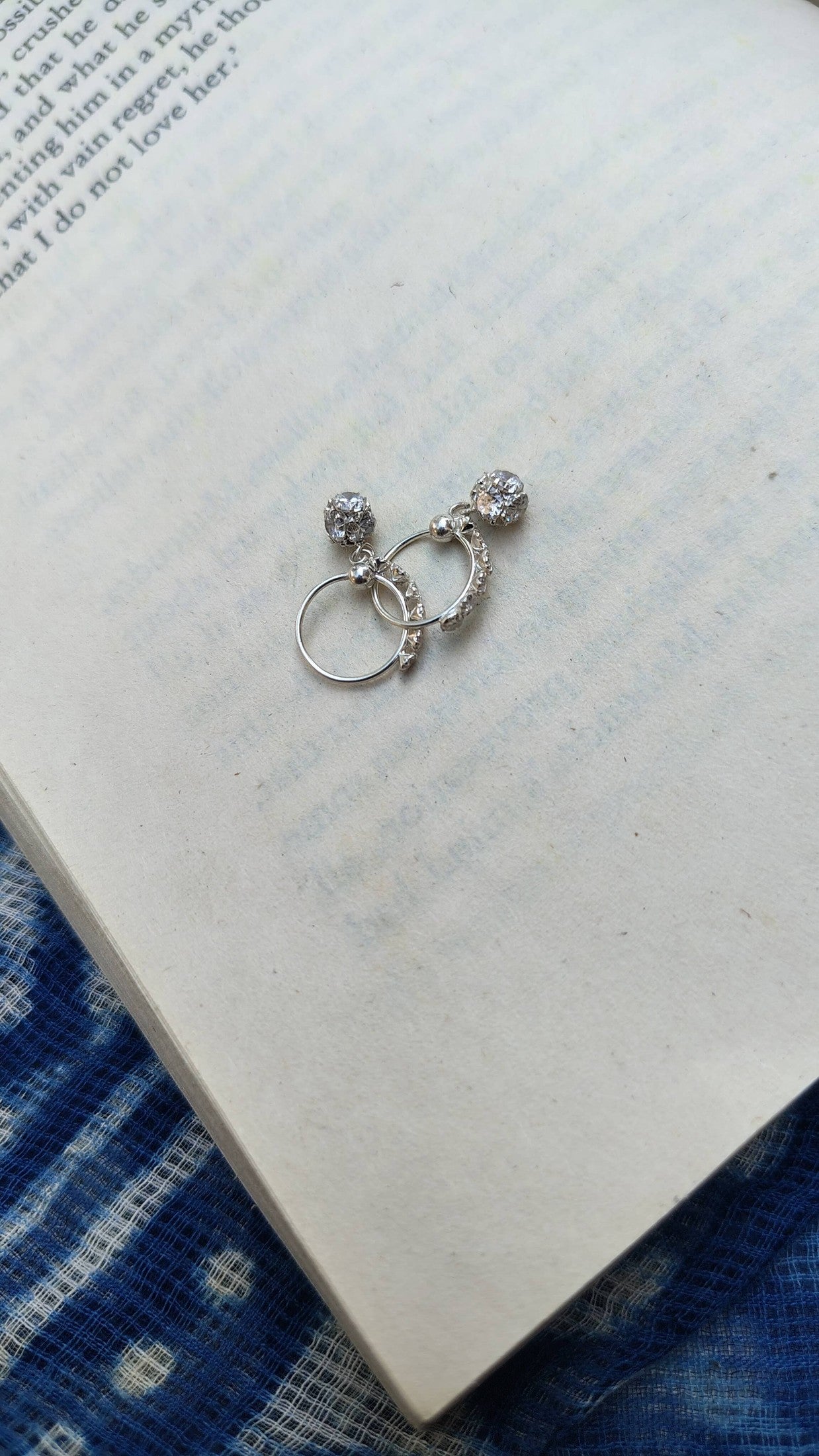 Silver earrings on an open book with a blue fabric background | Sadabahaar Jewelry