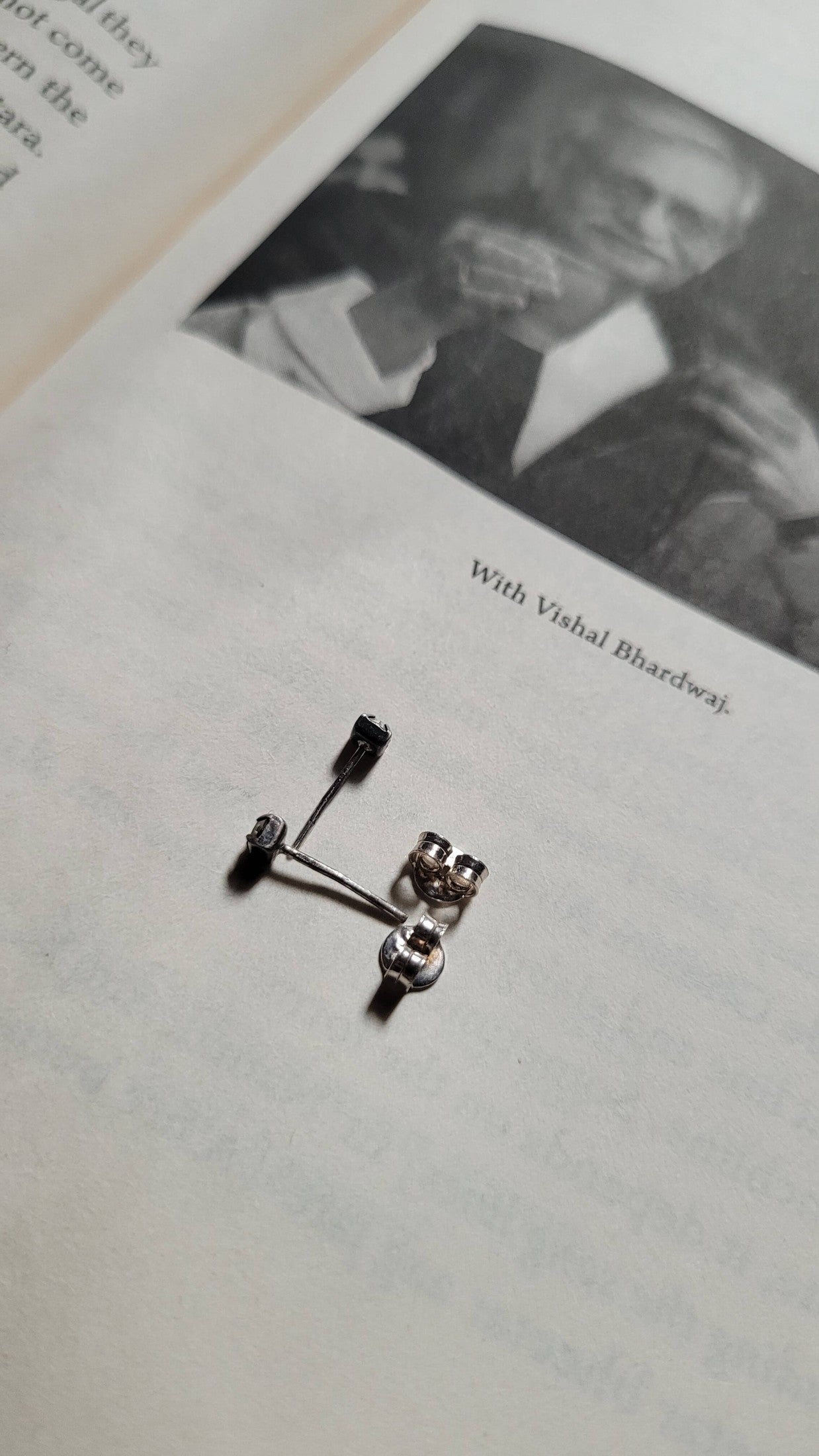 Silver earring on a book page with a black and white photo of a person in the background.