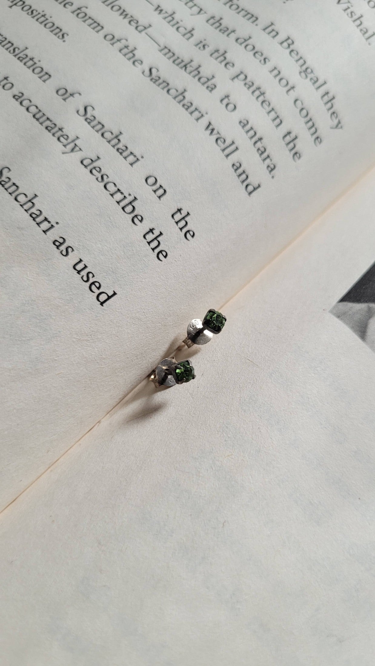 Silver earring with green gemstones on an open book