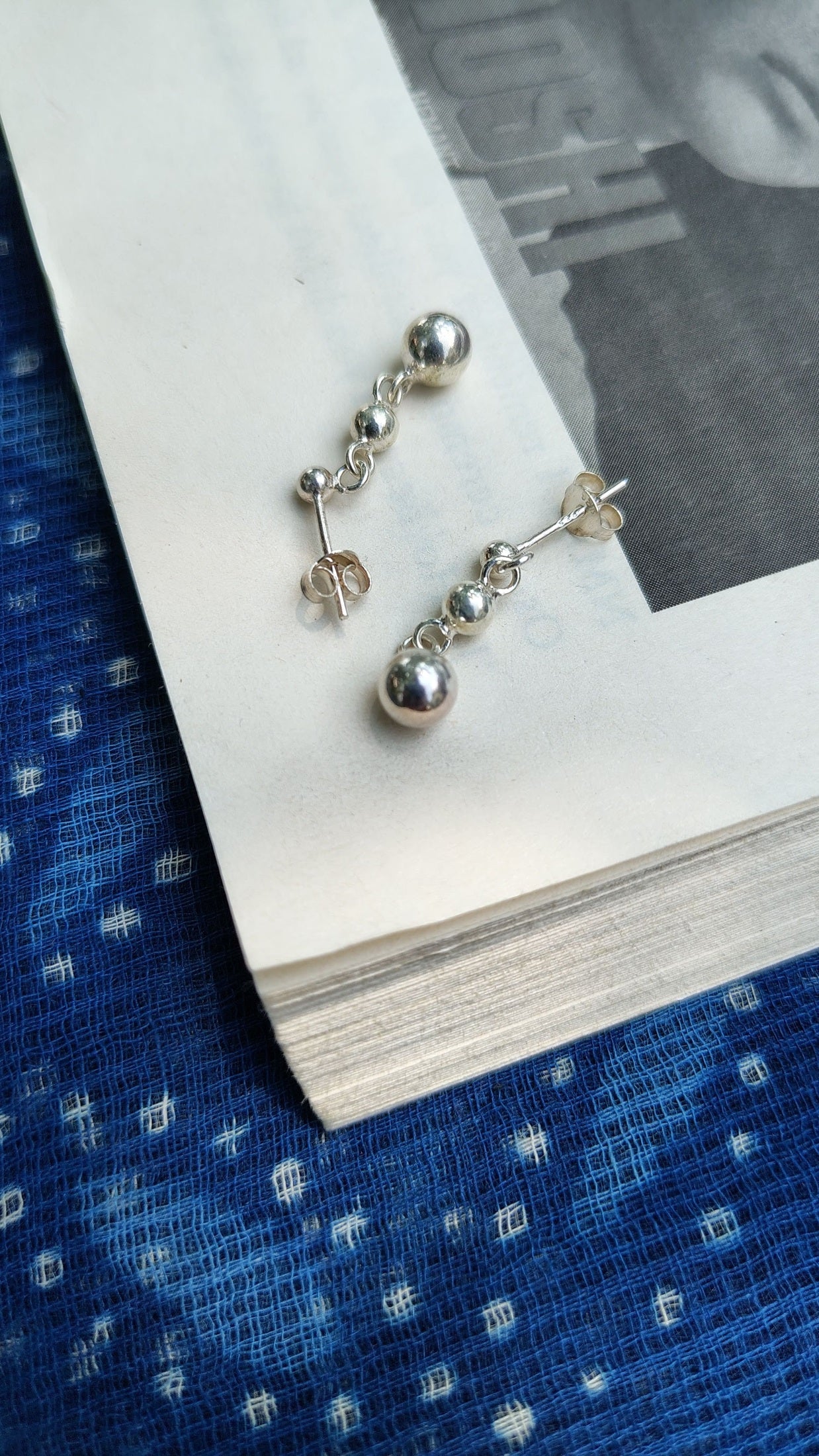 Silver ball earrings on an open book with a blue patterned fabric background