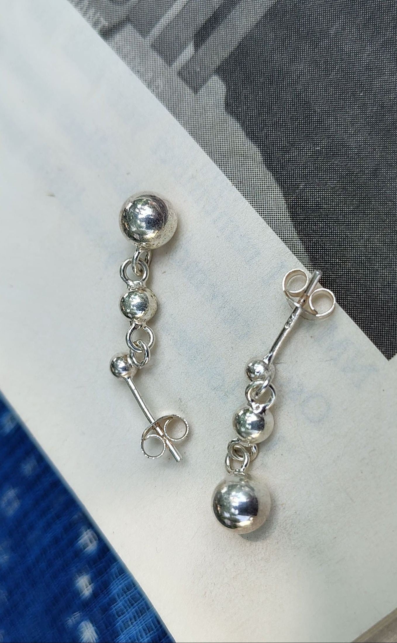 Silver earrings on a white surface with a blue fabric background
