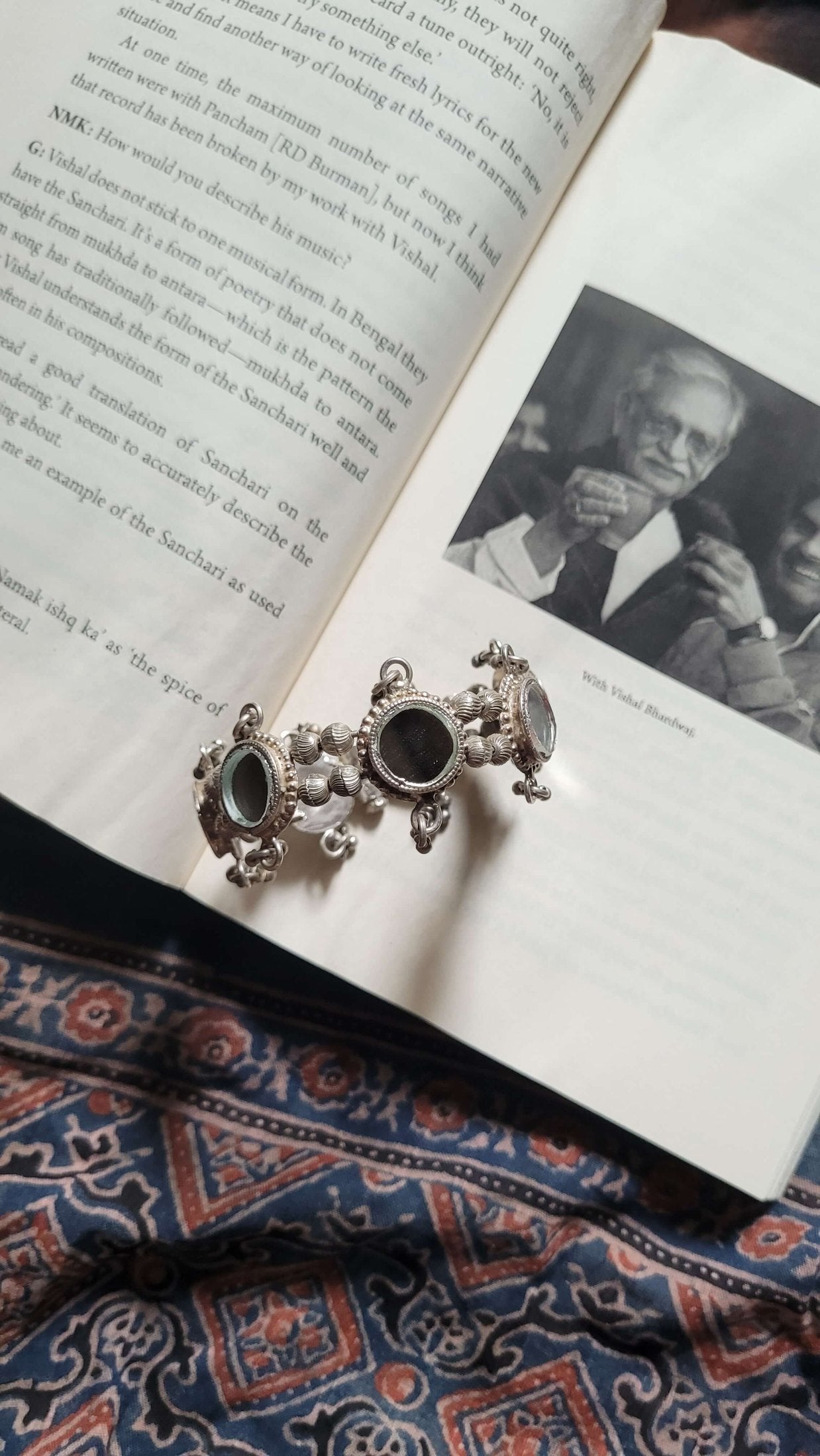 Silver Dhruvnanda Kada with black stones on an open book with a black and white photo inside.
