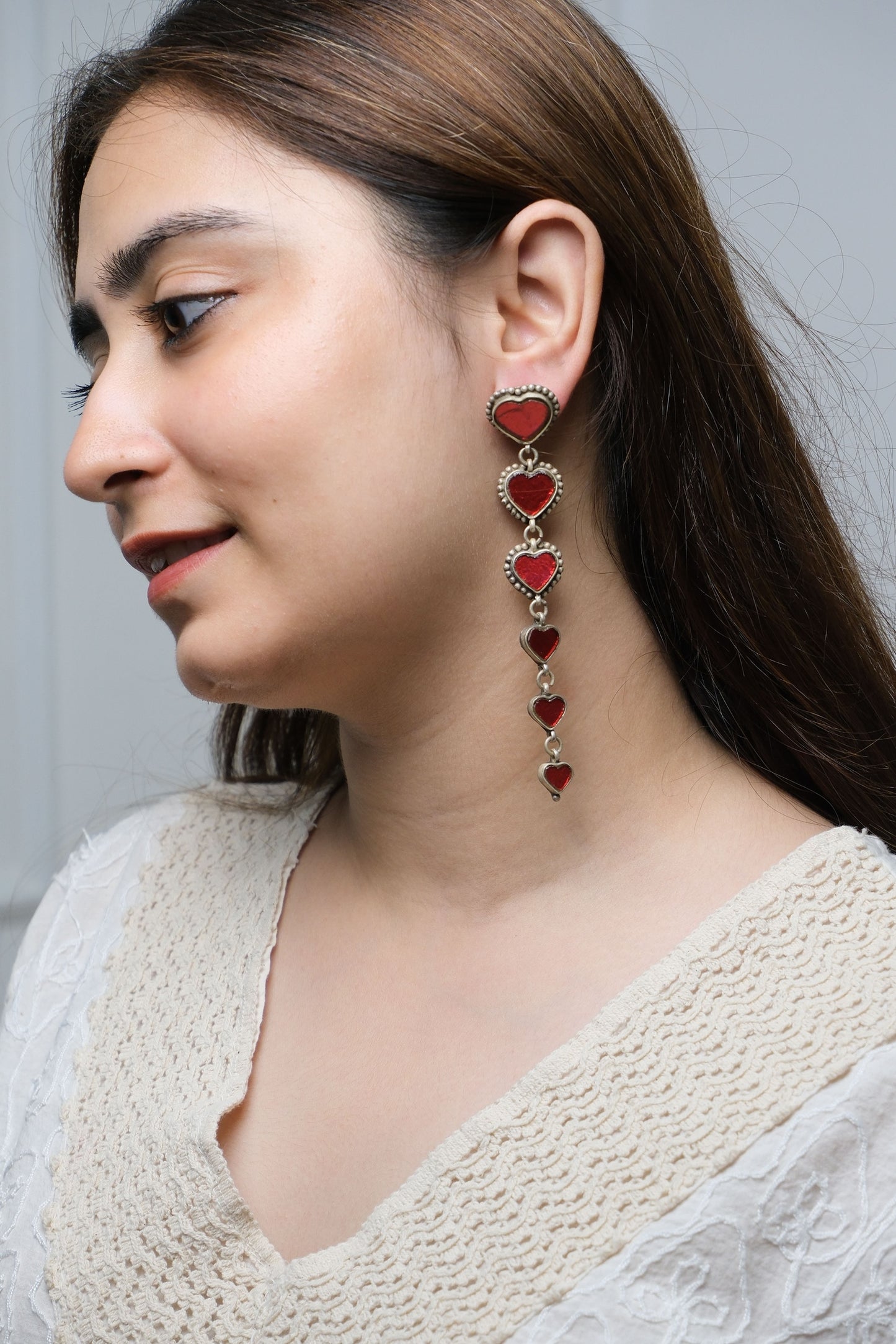 Woman wearing a delicate earrings with red heart pendants on a neutral background