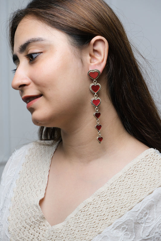 Woman wearing a delicate earrings with red heart pendants on a neutral background