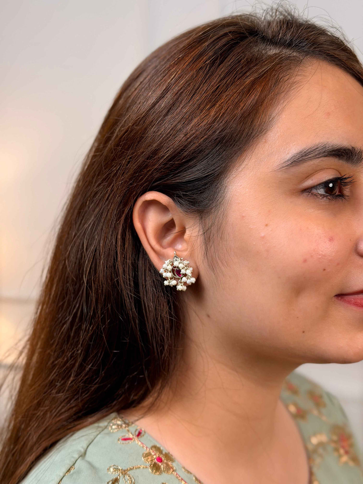 A close-up side profile of a woman wearing a small cluster earring with white pearls on her earlobe.