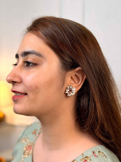 A close-up side profile of a woman with long brown hair wearing a silver-toned earring adorned with white stones and small pink accents.