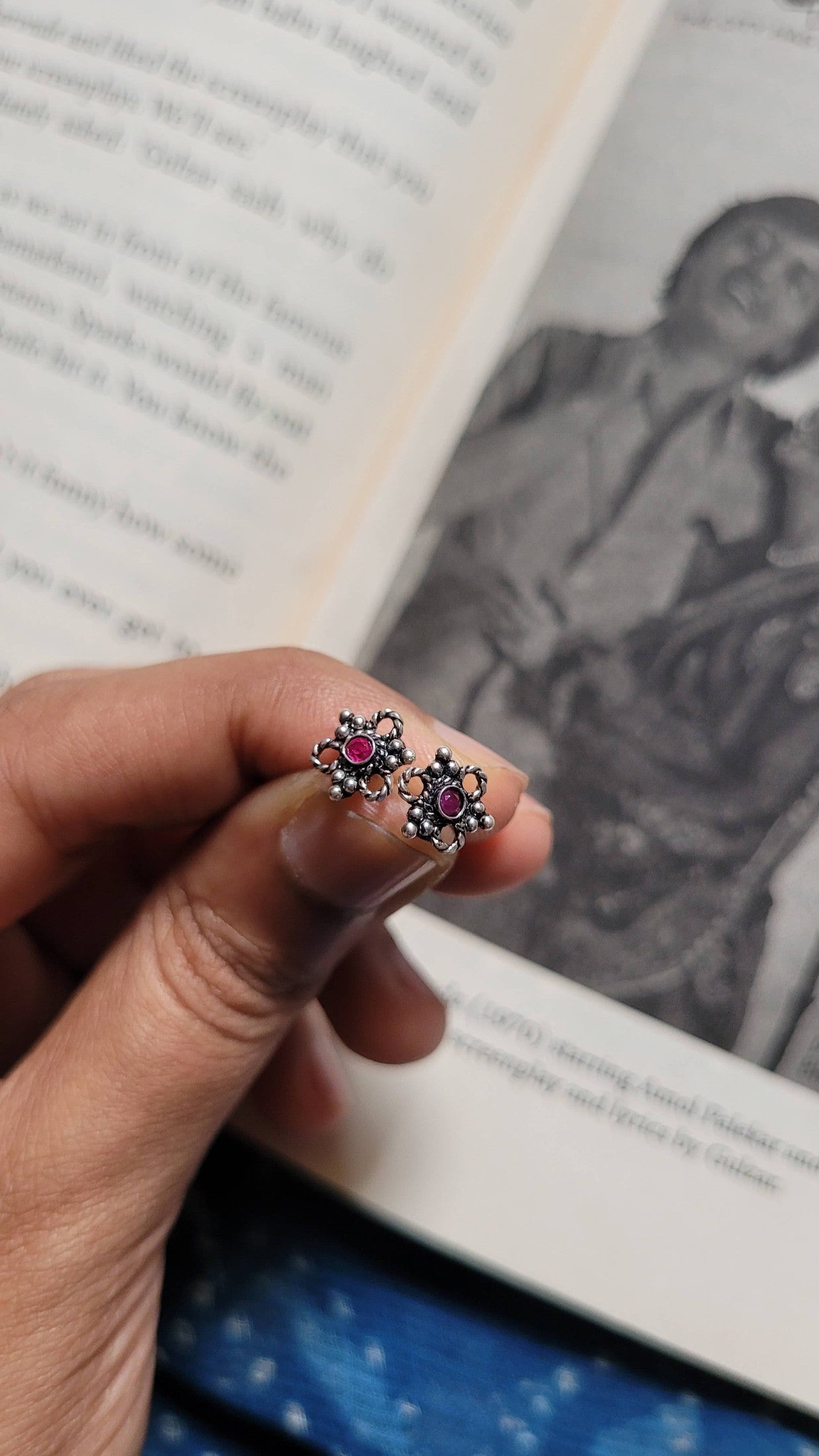 Close-up of a hand holding a pair of Eros Studs with gemstones against an open book.