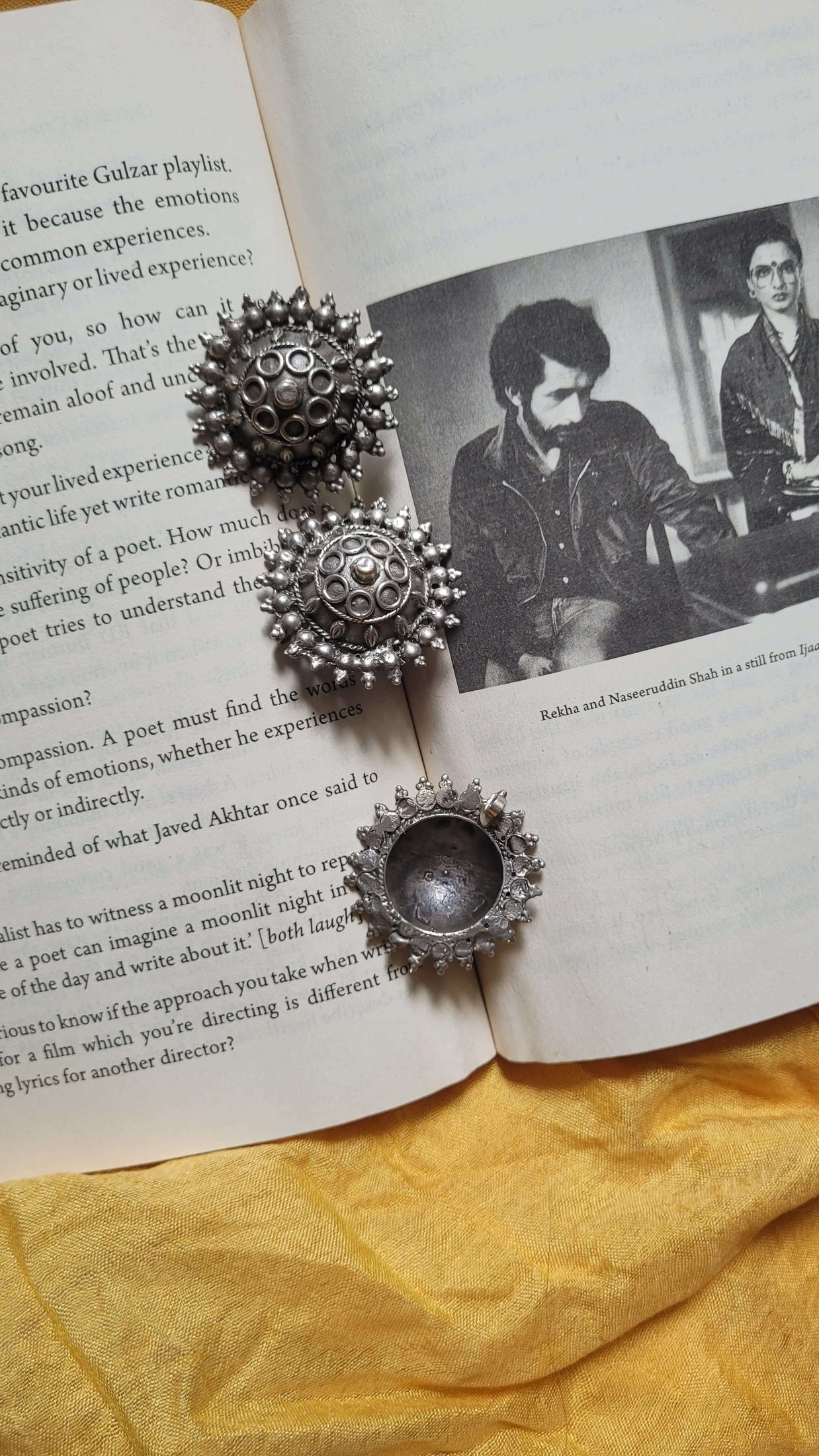 Silver earrings and pendant on an open book with a yellow fabric background
