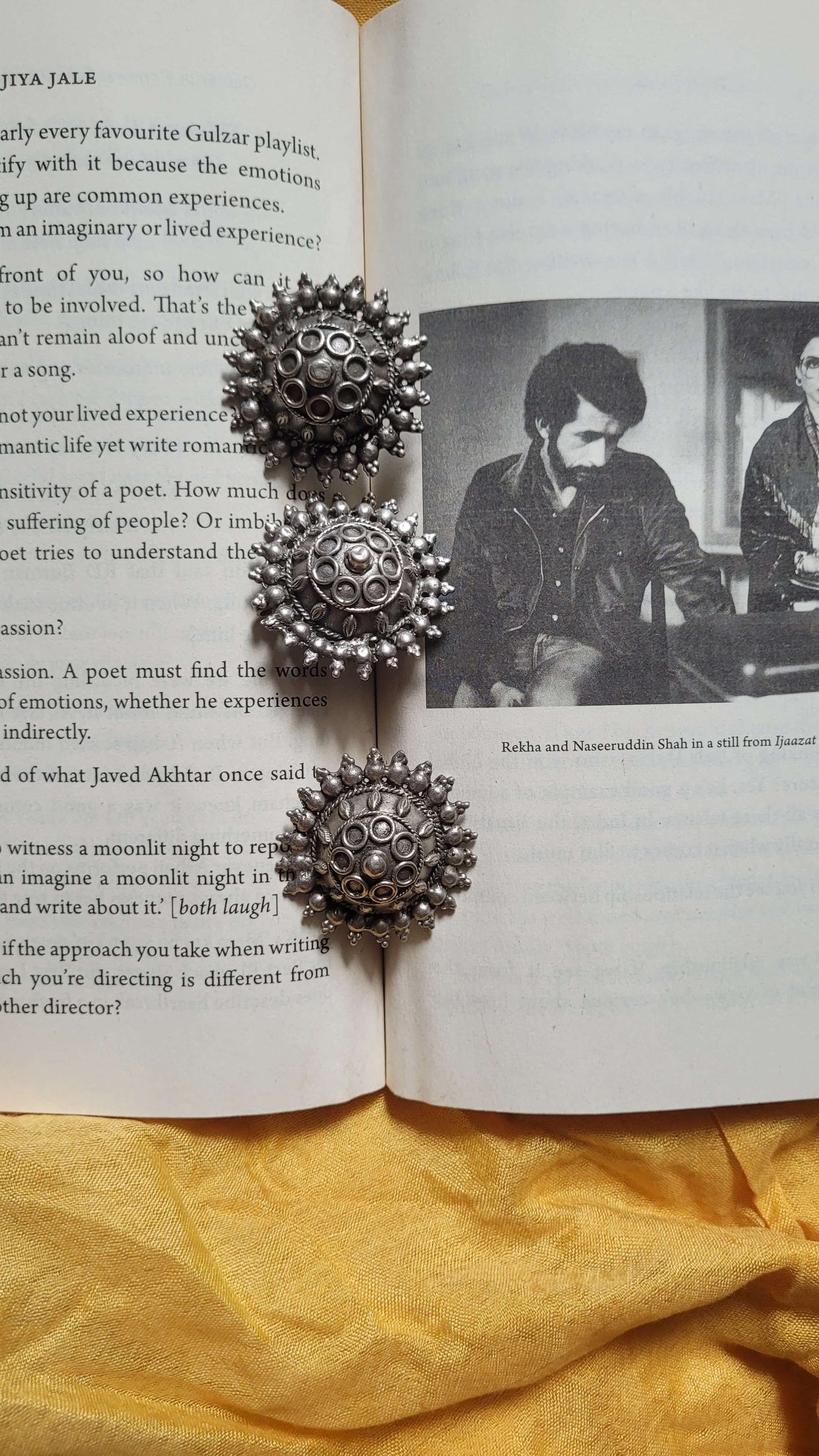 Gayatri Pendant and silver earrings on an open book with a yellow fabric background