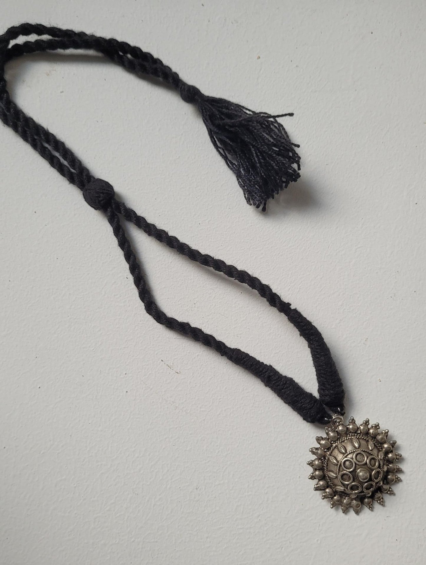 Black braided necklace with a textured silver pendant on a light gray background