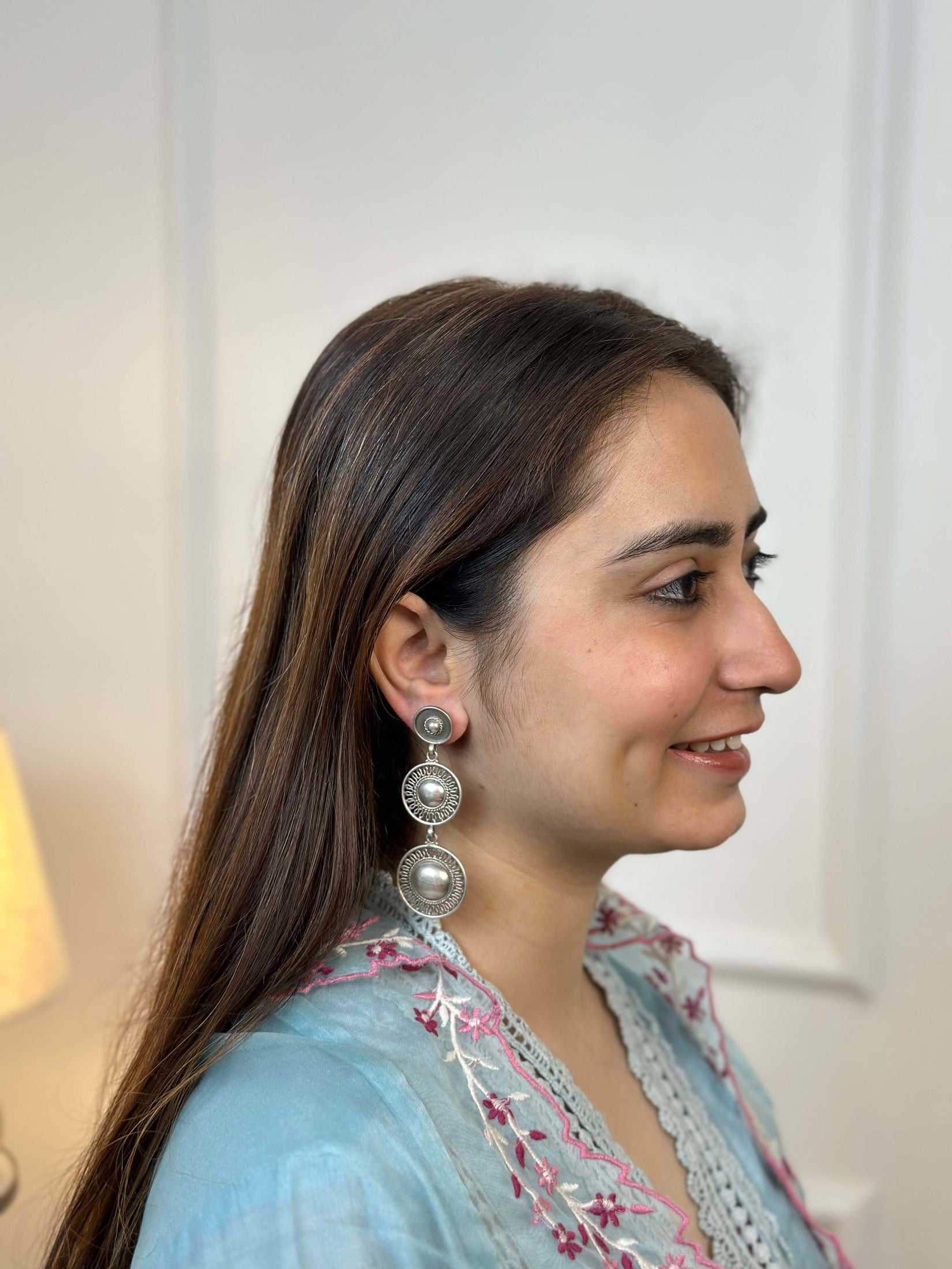Woman wearing silver earrings with a light blue and pink traditional outfit.
